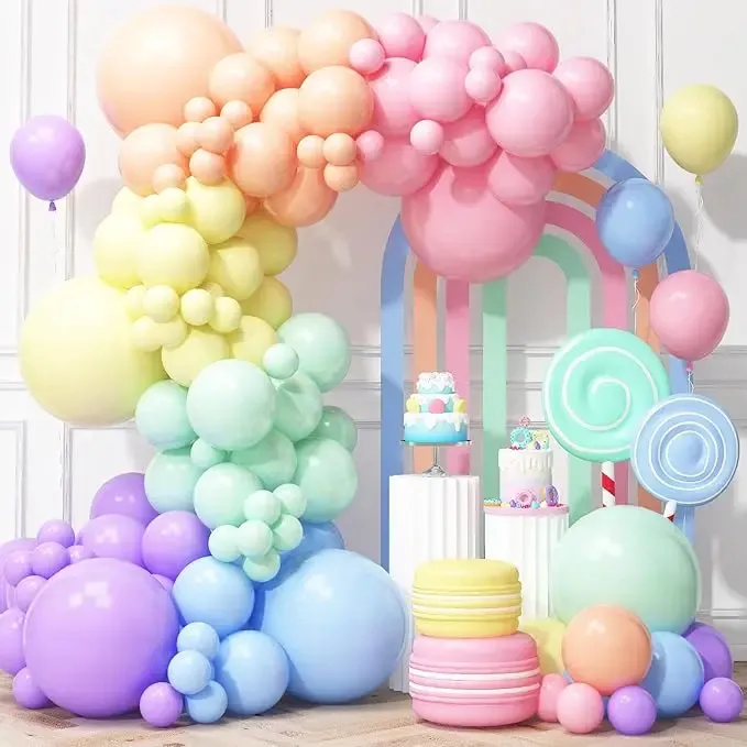 Prezentare eleganta pentru un set arcada baloane aniversare Macaron Pastel multicolor, montat asimetric langa un candy bar cu tematica dulciuri.