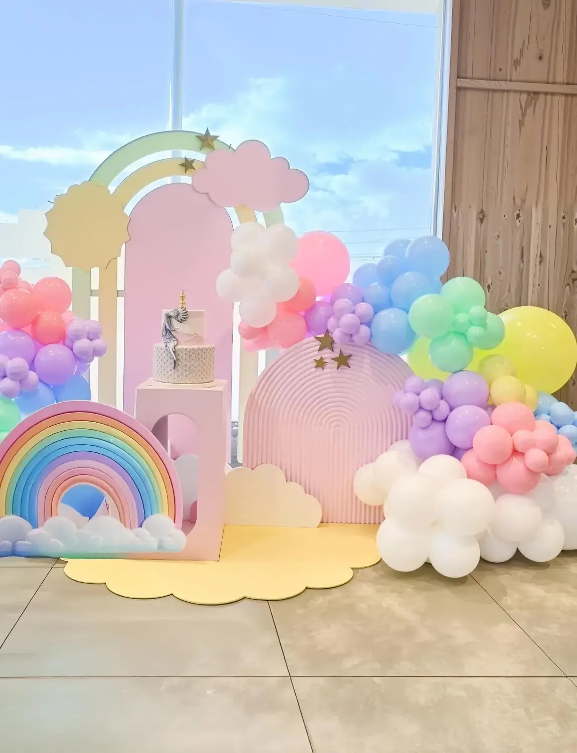 Prezentare eleganta pentru un set arcada baloane aniversare Macaron Pastel multicolor, montat asimetric langa un candy bar cu tematica dulciuri.