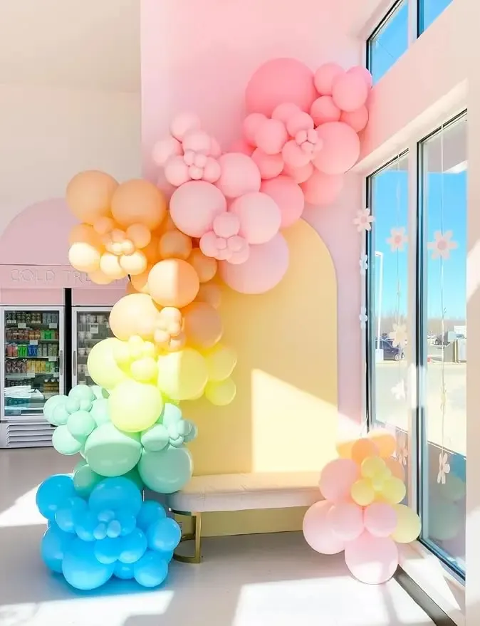 Prezentare eleganta pentru un set arcada baloane aniversare Macaron Pastel multicolor, montat asimetric langa un candy bar cu tematica dulciuri.