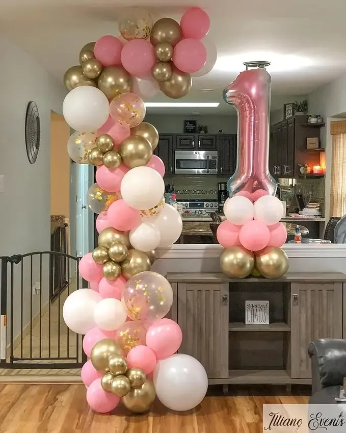 Prezentare eleganta pentru un set arcada baloane aniversare roz si alb, decorat asimetric cu baloane aurii si transparente cu confetti.