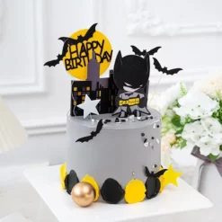Set de decoratiuni pentru tort cu tema Batman, incluzand silueta neagra a orasului, luna galbena cu Happy Birthday si personajul decorativ.